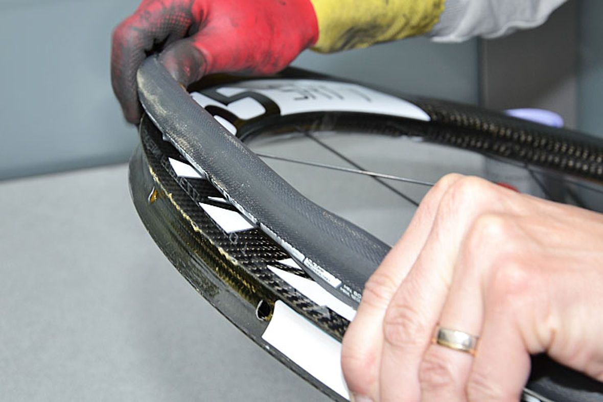 Endgültige Reifenmontage: Zuerst wird der ganz leicht aufgepumpte Reifen am Ventil sauber und gerade auf die Felge gesetzt. Dann arbeitet man sich beidseitig weiter, bis nur noch das letzte Reifenstück (gegenüber des Ventils) über die Felge muss.